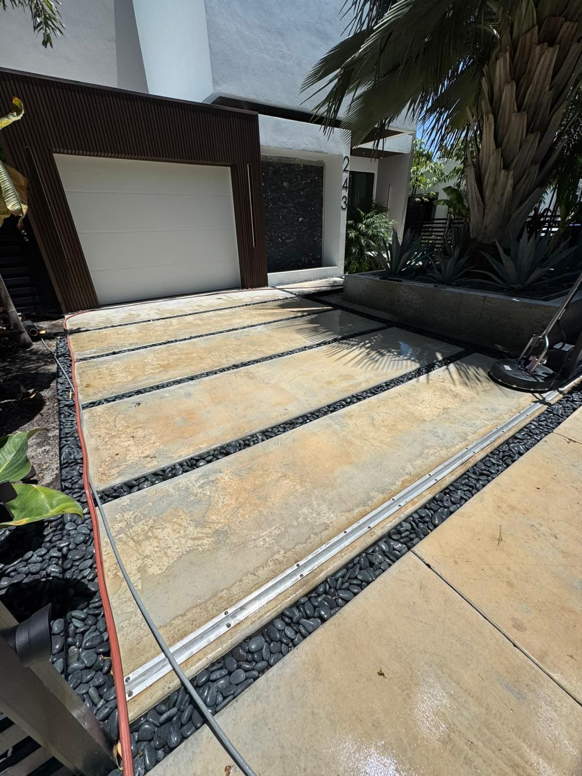 Concrete driveway with black gravel borders, leading to a modern house with a garage.