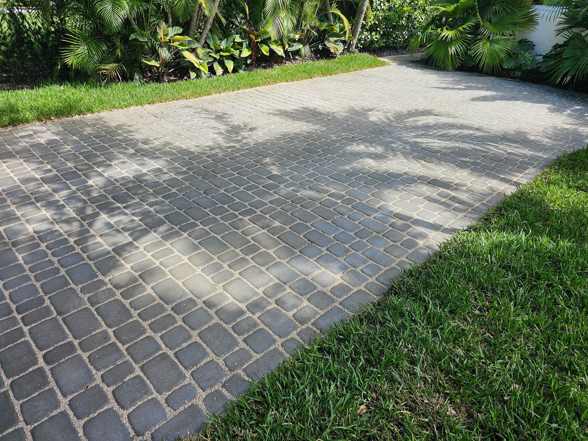 Brick paved driveway with green grass borders, sunlight dappled.