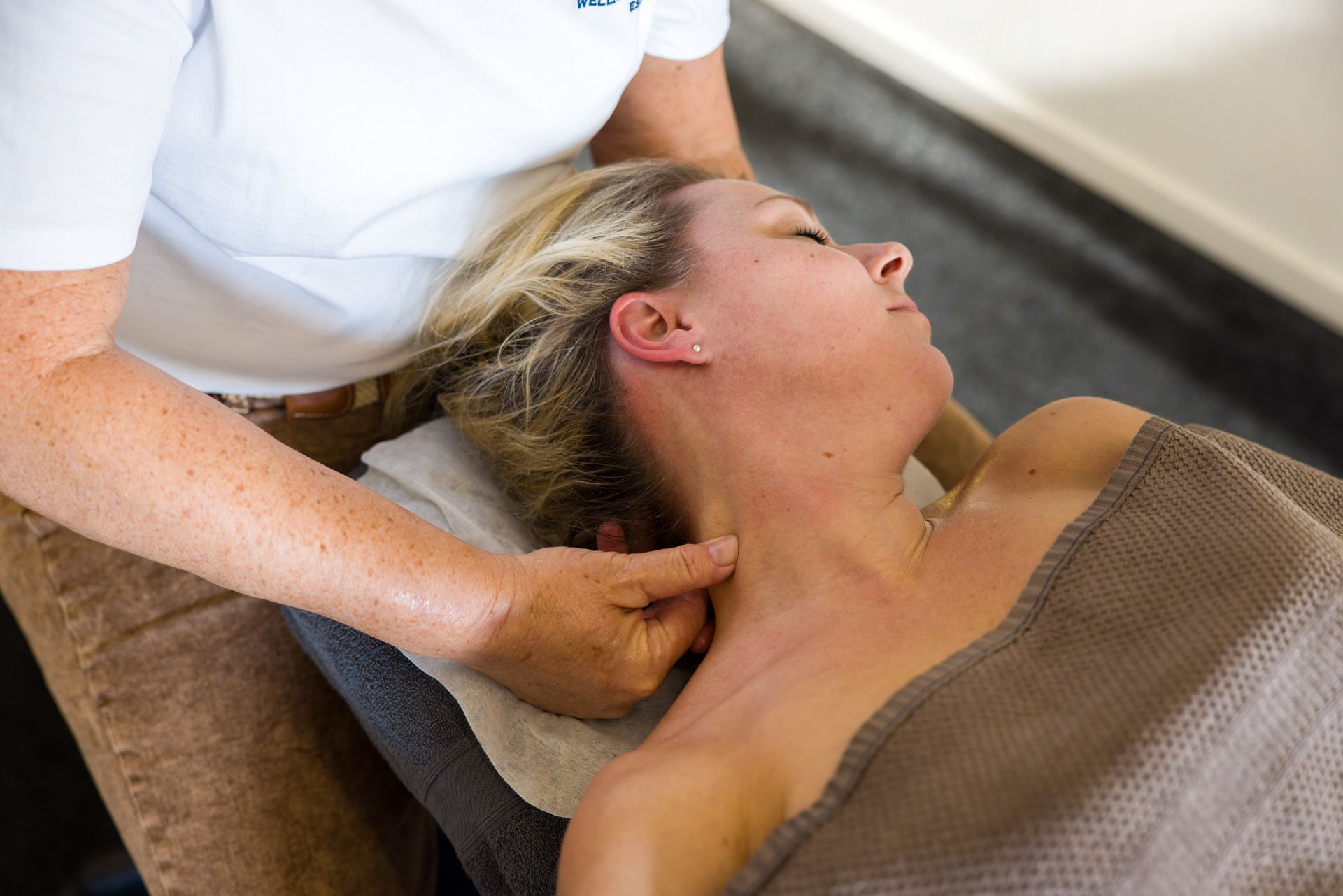 Persoon die een nekmassage krijgt; handen op de nek, spa-omgeving.