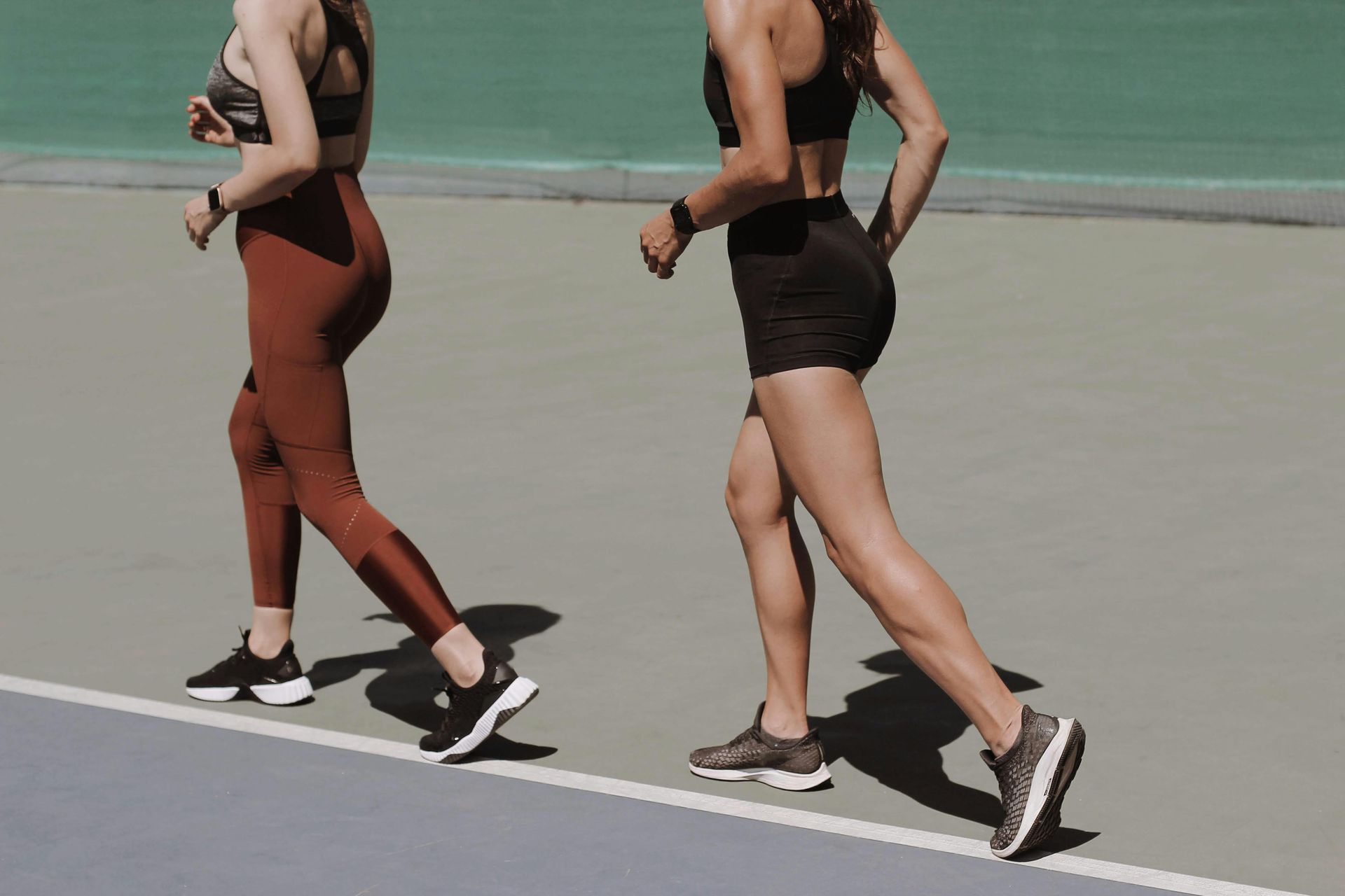 Twee mensen rennen op een atletiekbaan, de een in een rode legging, de ander in een zwarte korte broek, met hardloopschoenen.