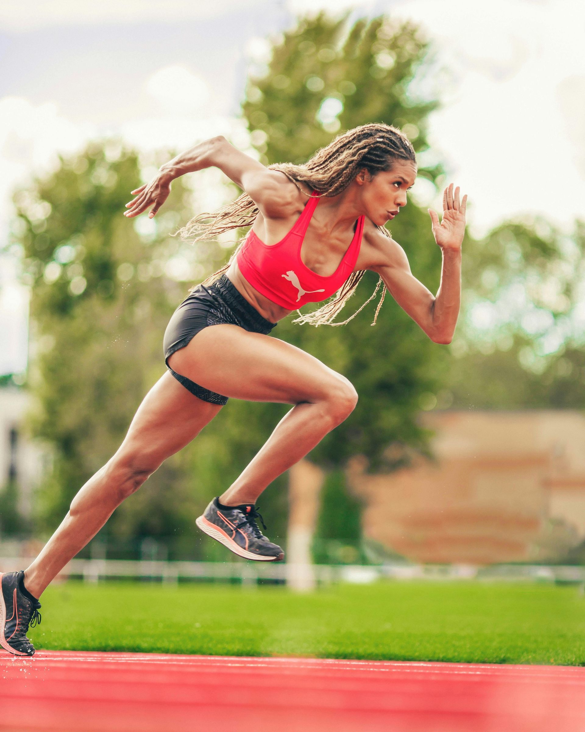 Athlete running on a red track, wearing a red top and black shorts.