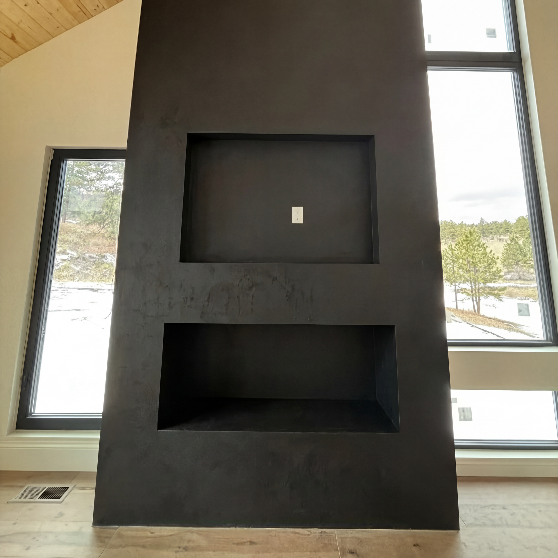 A dark matte fireplace feature wall with a built-in recessed television niche and a lower open fireplace box.