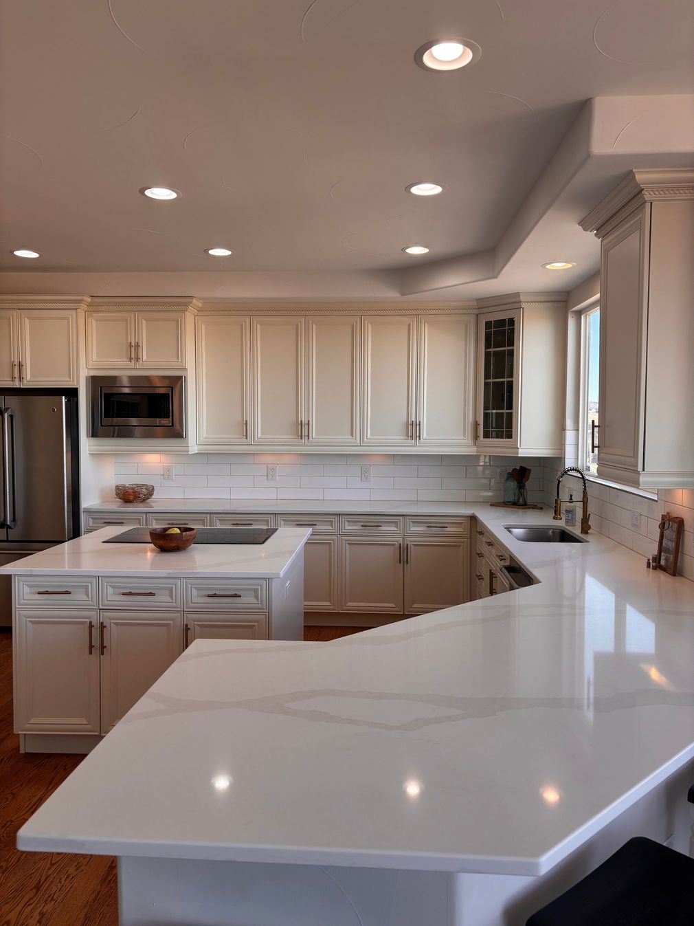 A modern, white kitchen with a large island and countertops, stainless steel appliances, and built-in cabinetry.