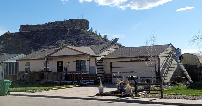 House with attached garage in foreground, large rock formation in the background under blue sky.