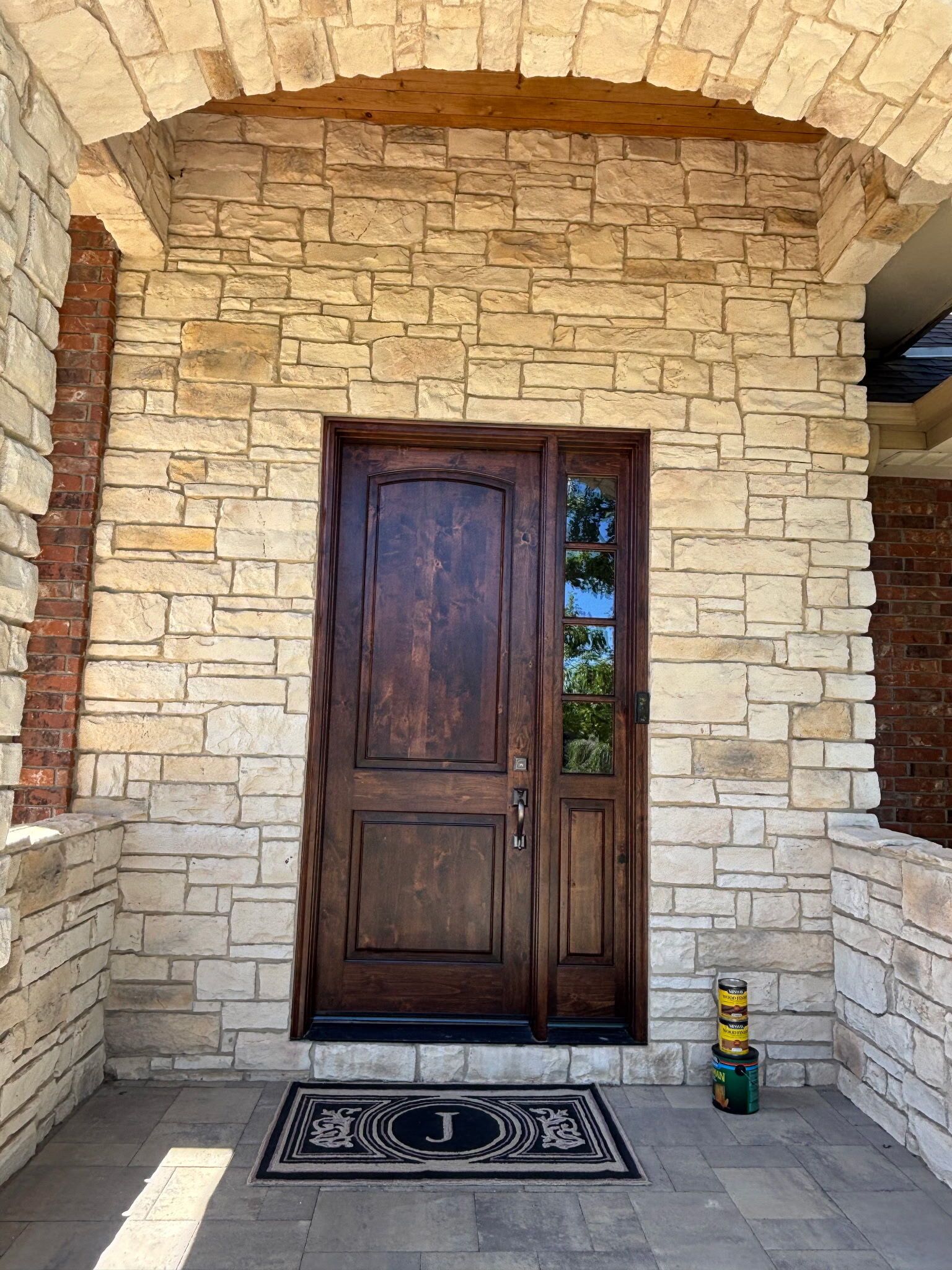 Wooden front door set in a stone entryway with a doormat and small lantern on the porch.