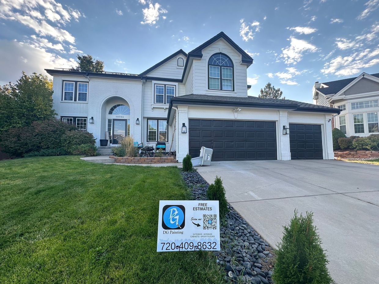 Two-story white house with black garage doors, arched window, and sign on front lawn.