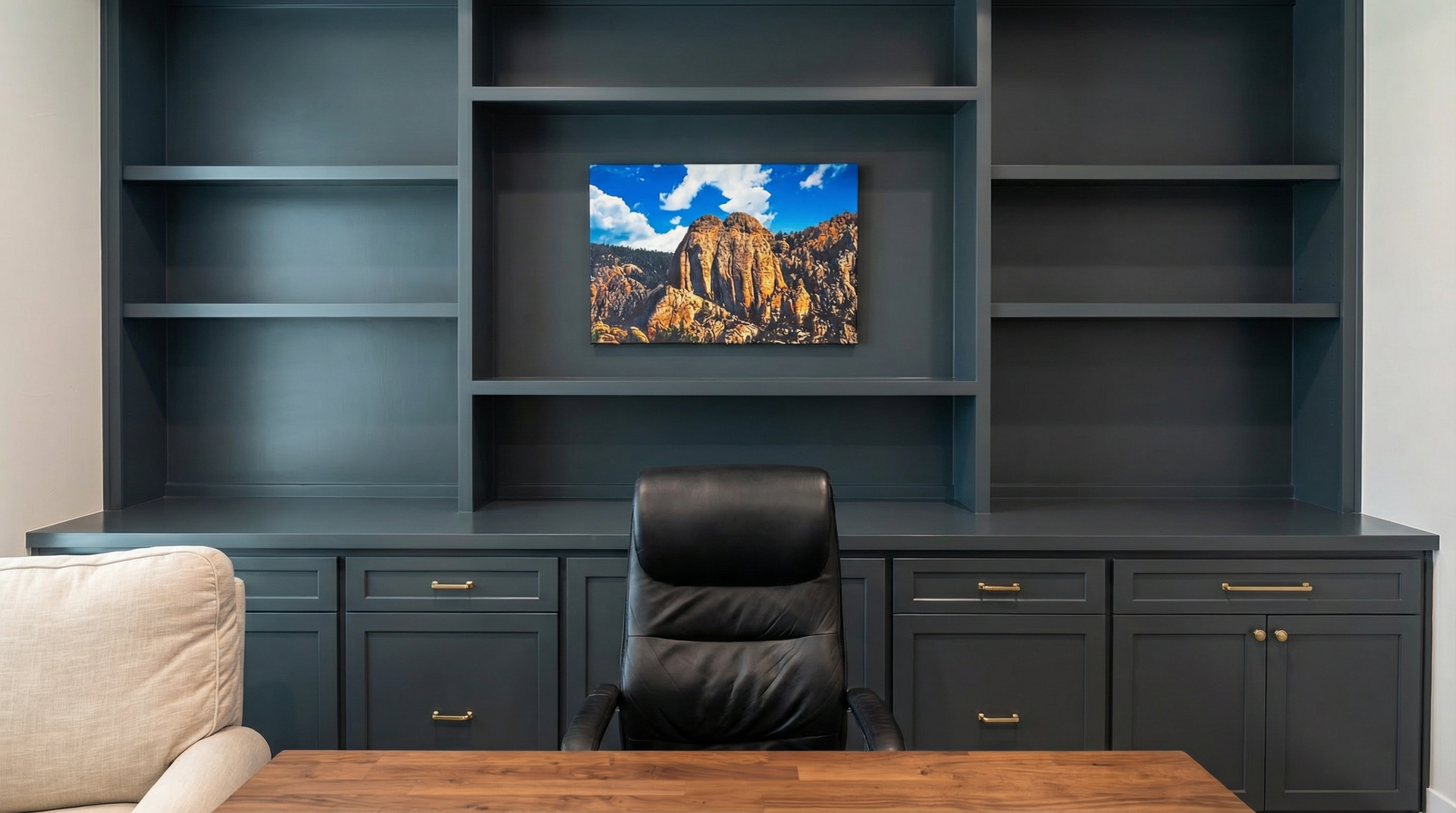 A home office with a desk , chair , shelves and pictures on the wall.