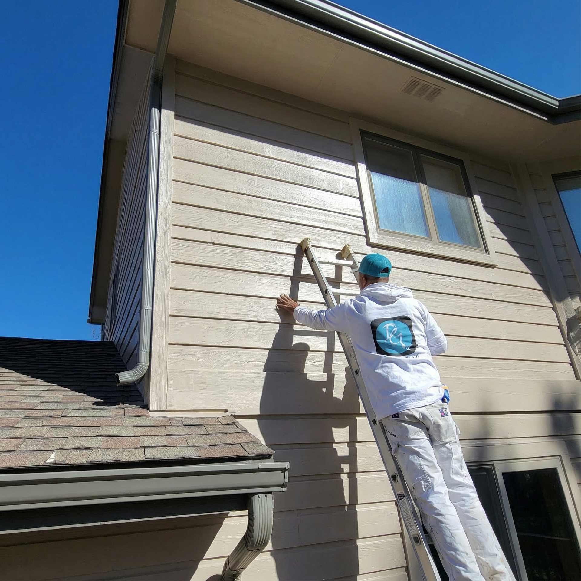 A man is painting the side of a house with a ladder.