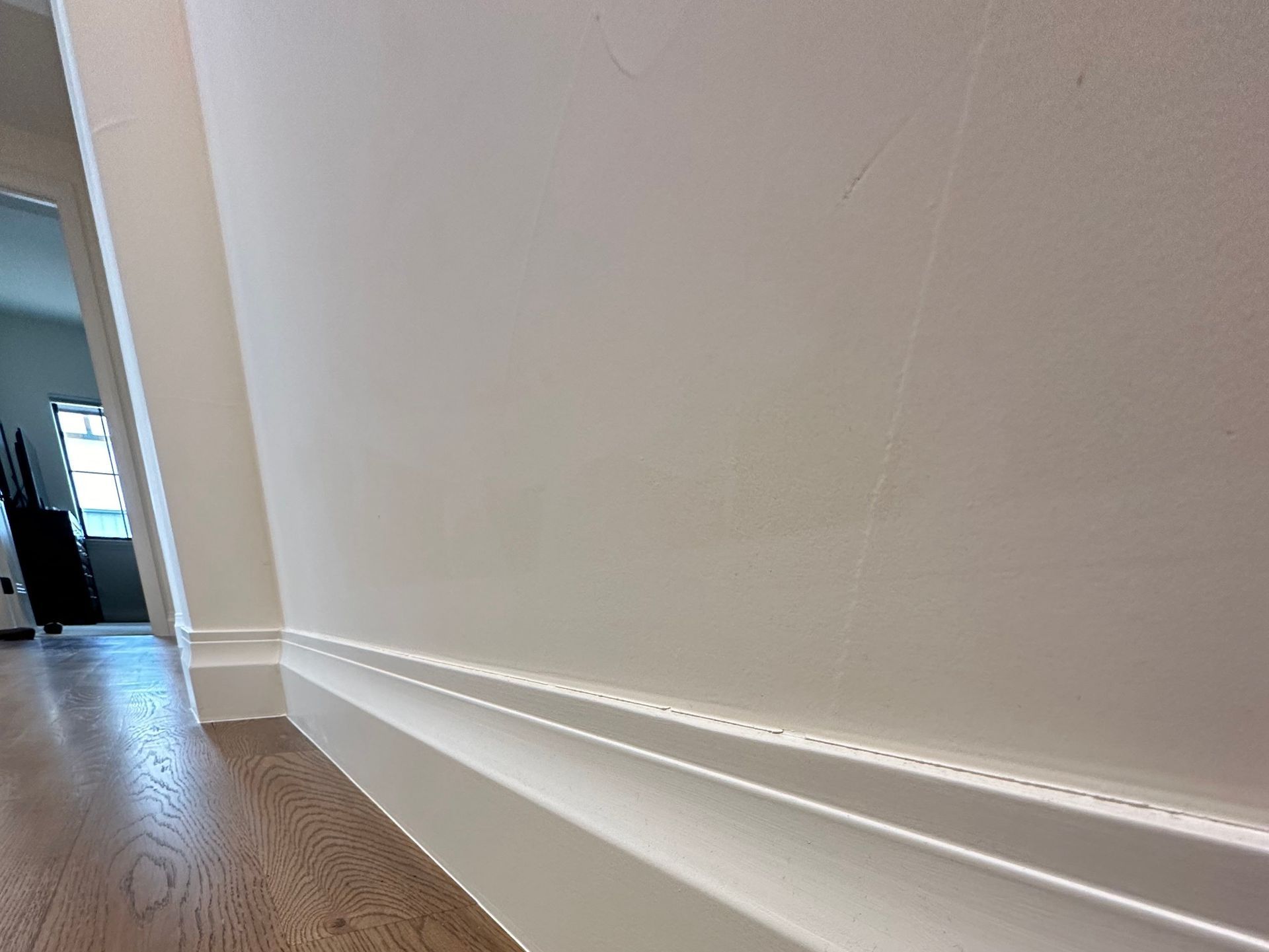 A white wall with a wooden floor in a hallway.