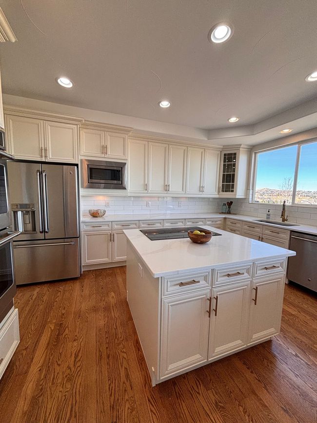 A kitchen with white cabinets, a central island with a stone countertop, stainless steel appliances, and wood flooring.