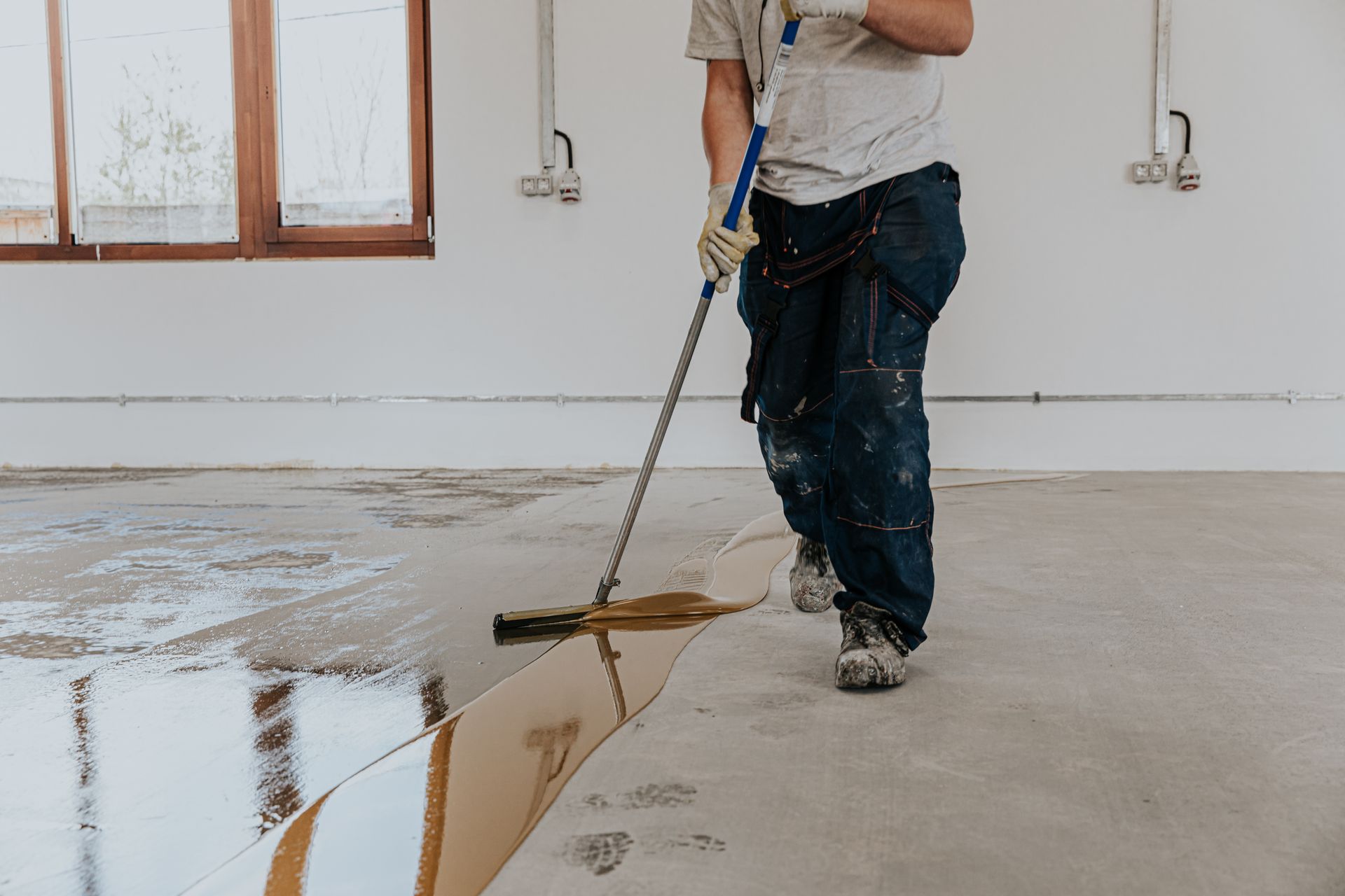 A man is painting a concrete floor with a mop.