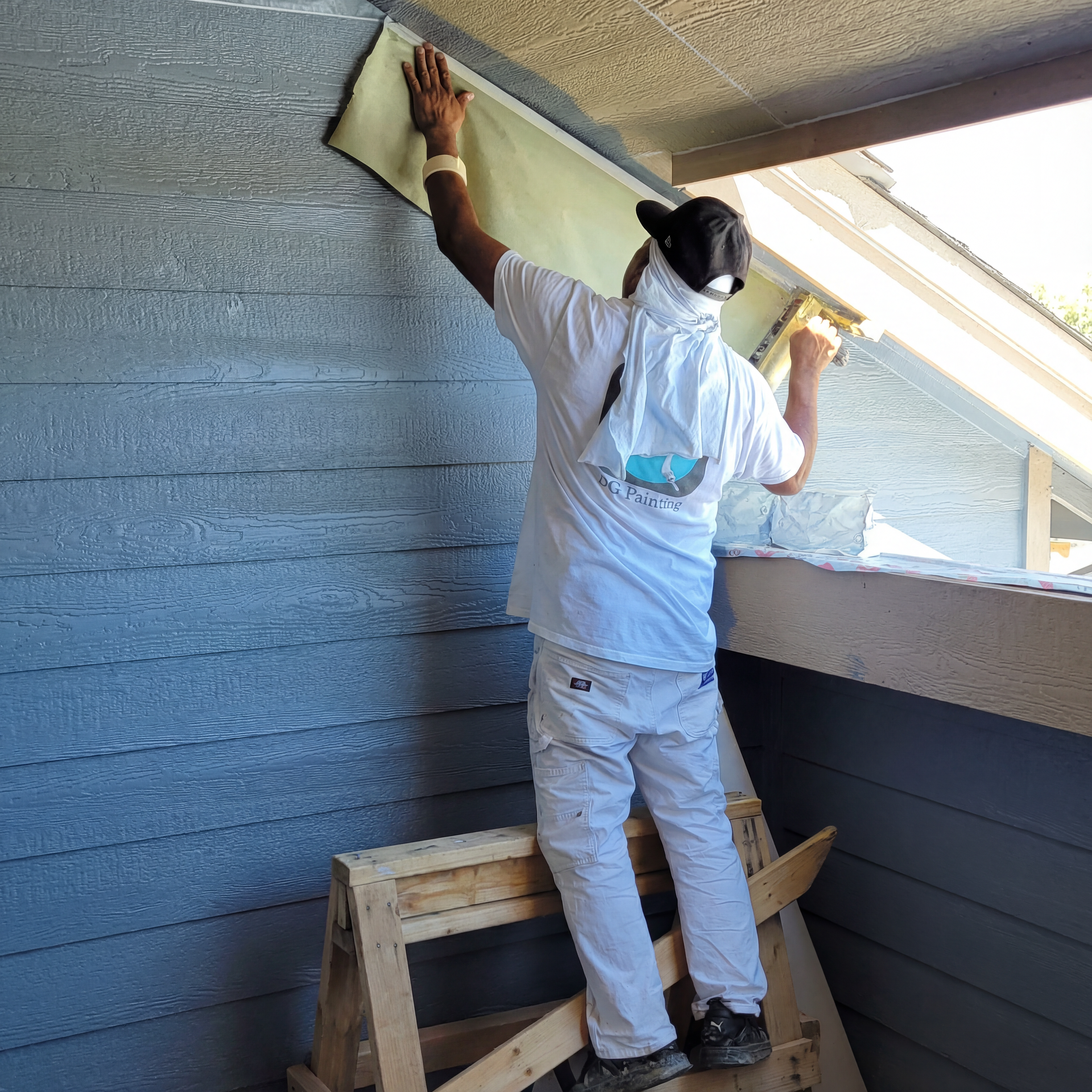 A man is standing on a wooden stool painting a wall.