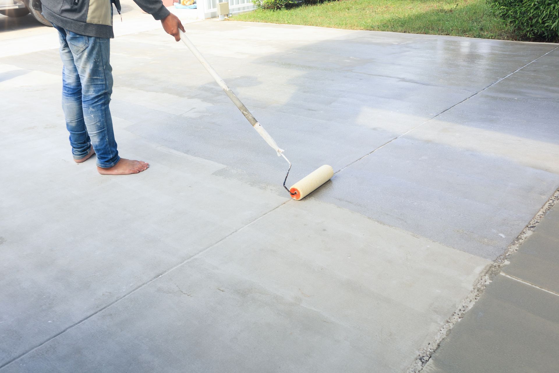 Person rolling paint onto concrete surface, outdoors.