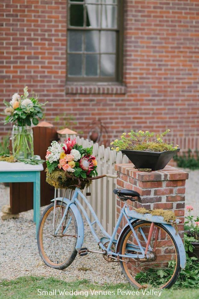 Vintage blue bicycle with flower baskets beside a brick house and teal table with flowers