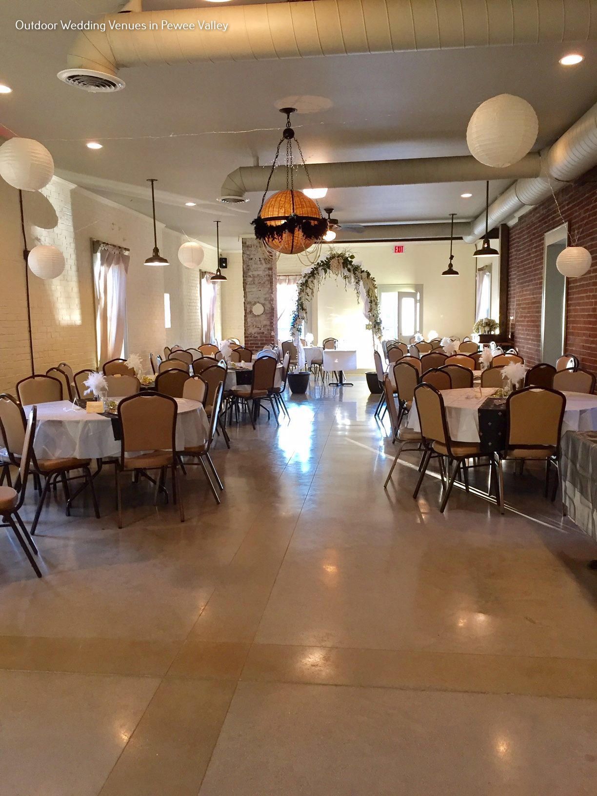 Wedding reception hall with round tables, white chair covers, and an arched floral entrance