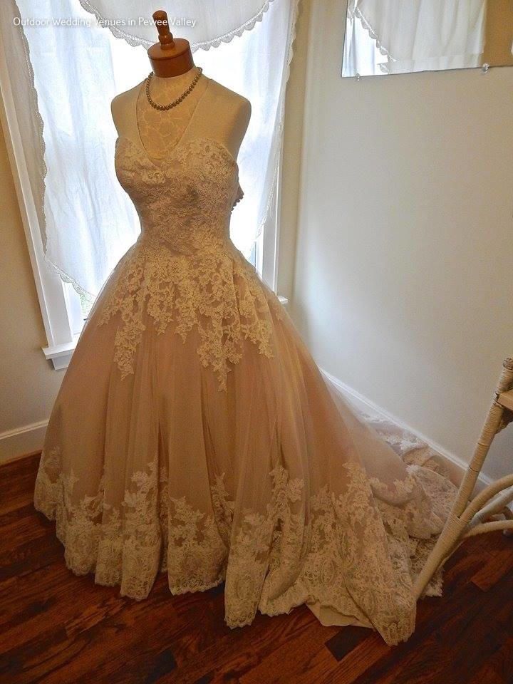 Ivory lace wedding dress on a mannequin by a window with sheer curtains