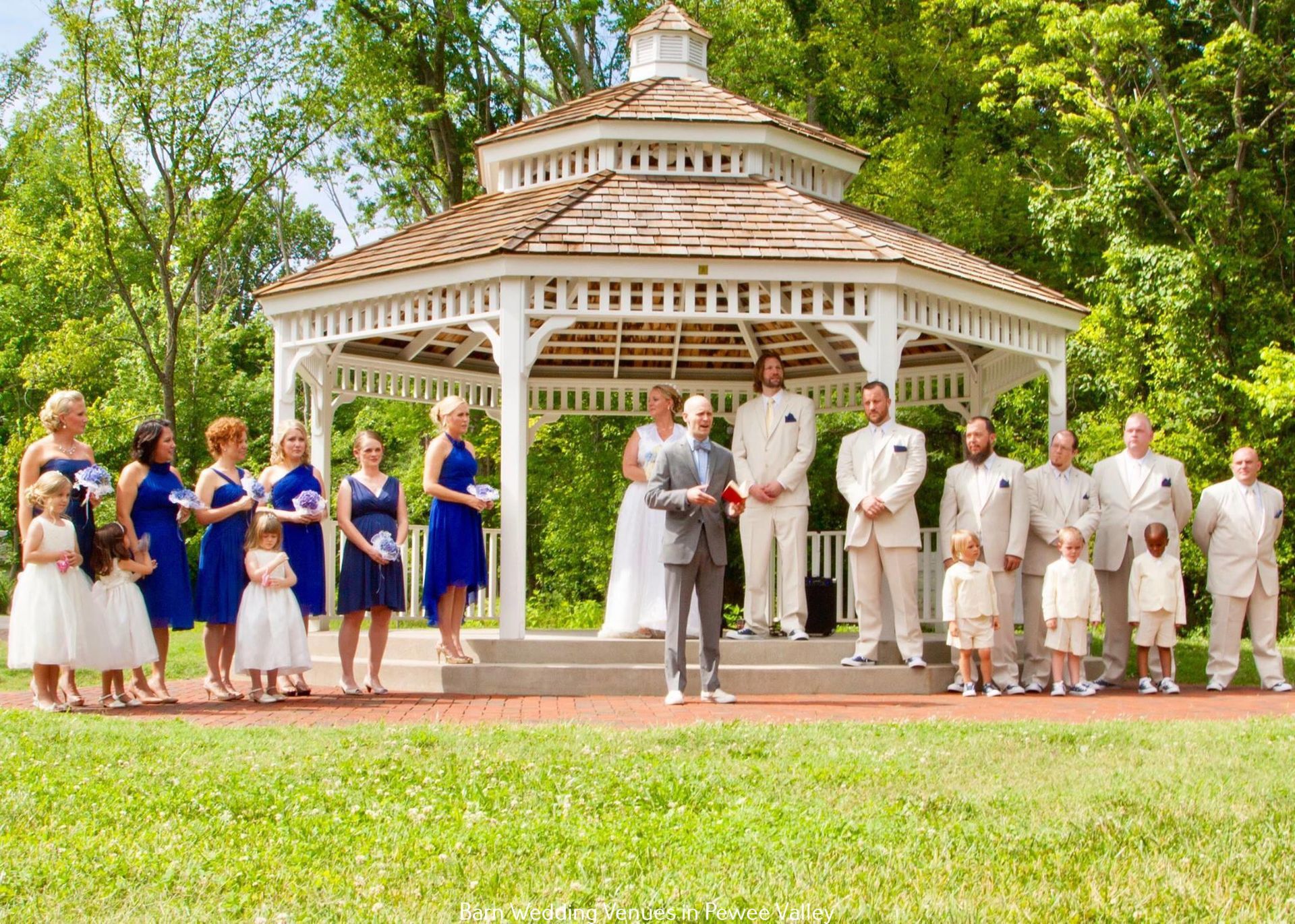 Wedding party gathered in front of a white gazebo in a green park