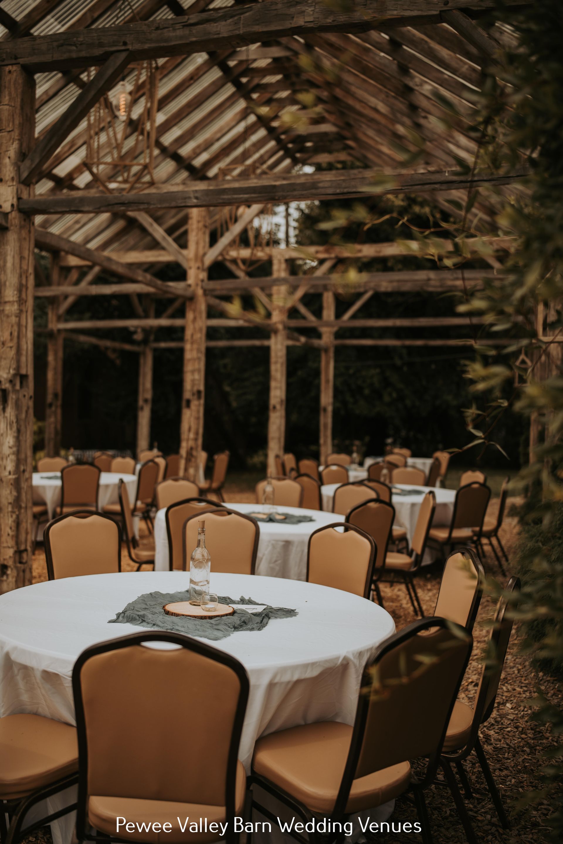 Rustic barn wedding reception with round tables, white tablecloths, and wooden chairs under a timber roof