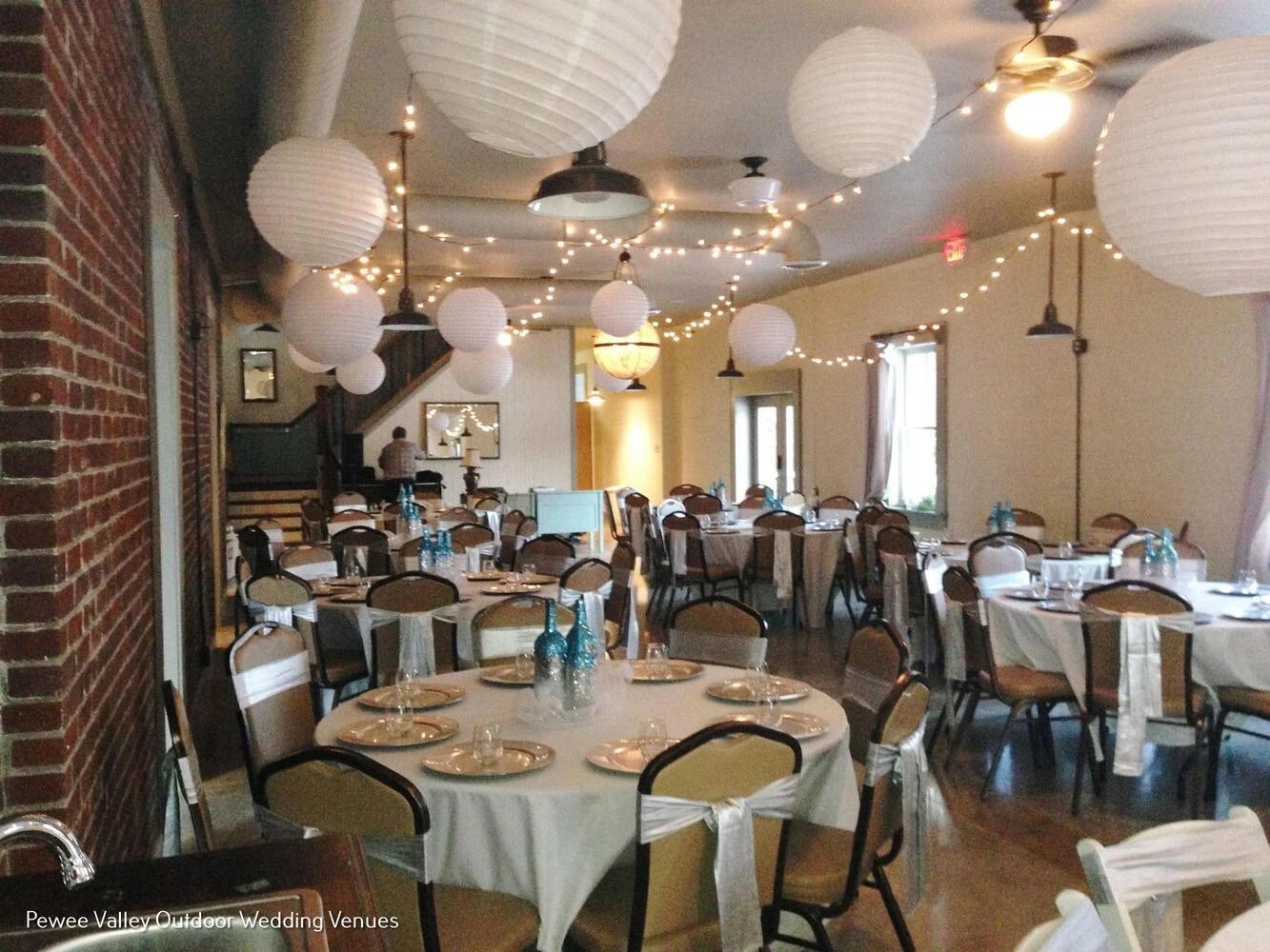 Reception hall set with round tables, paper lanterns, and string lights, empty and ready for guests