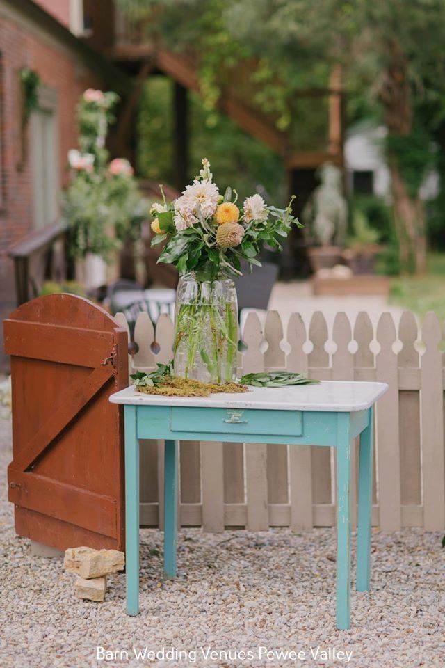Turquoise table with flower vase in a garden courtyard, beside a white picket fence and brick wall