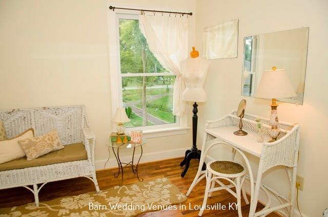 Bright cozy vanity room with wicker chair, white desk, mirror, and large window overlooking greenery