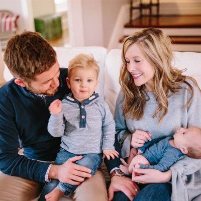 Family sitting together on a couch, with a man, a woman, two small children, and a baby in a cozy living room.