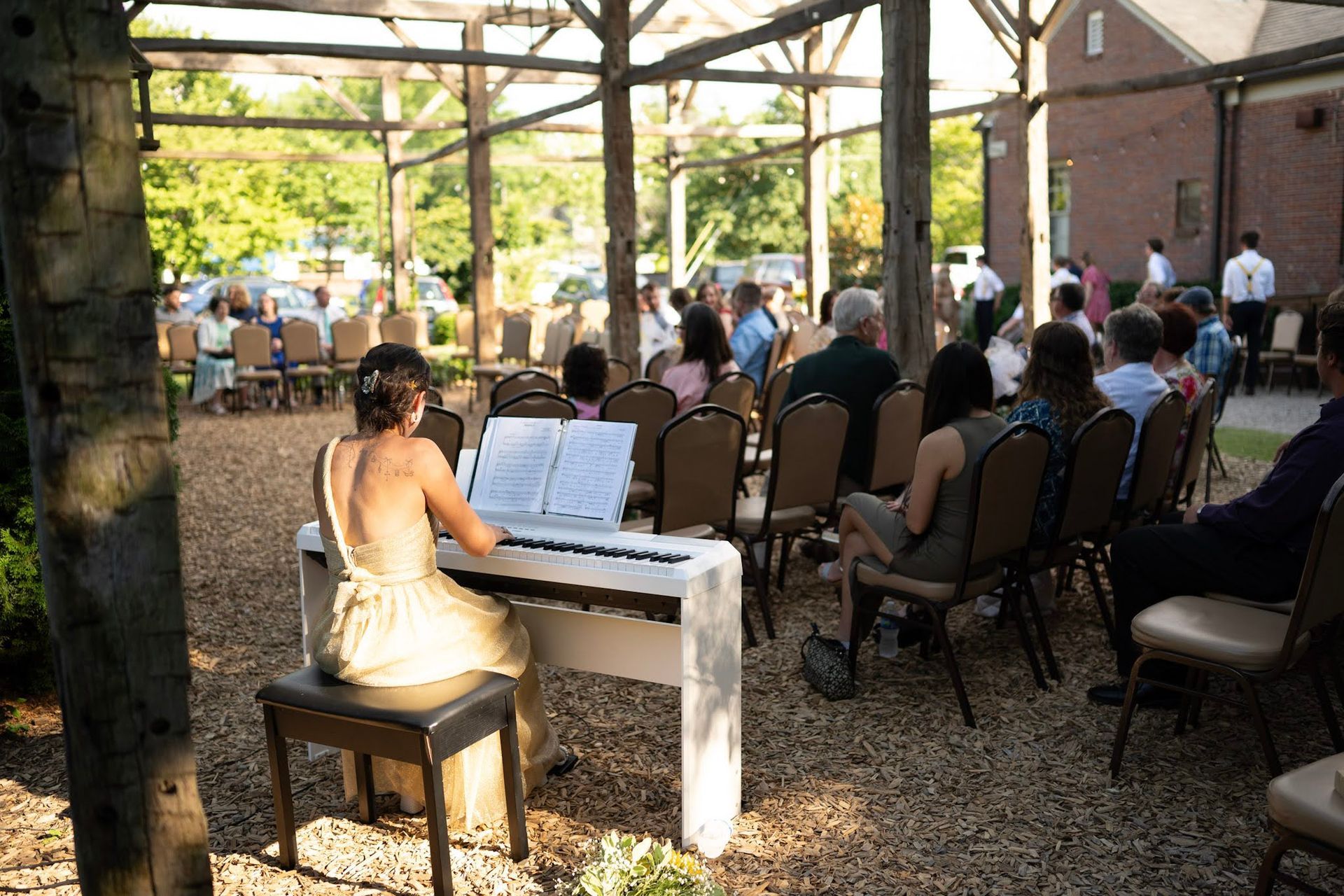 Pianist playing a white keyboard for seated guests at an outdoor wedding reception