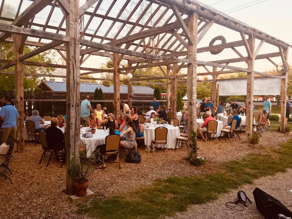 Outdoor wedding reception under a rustic wooden pavilion with guests seated at white-clothed tables at sunset