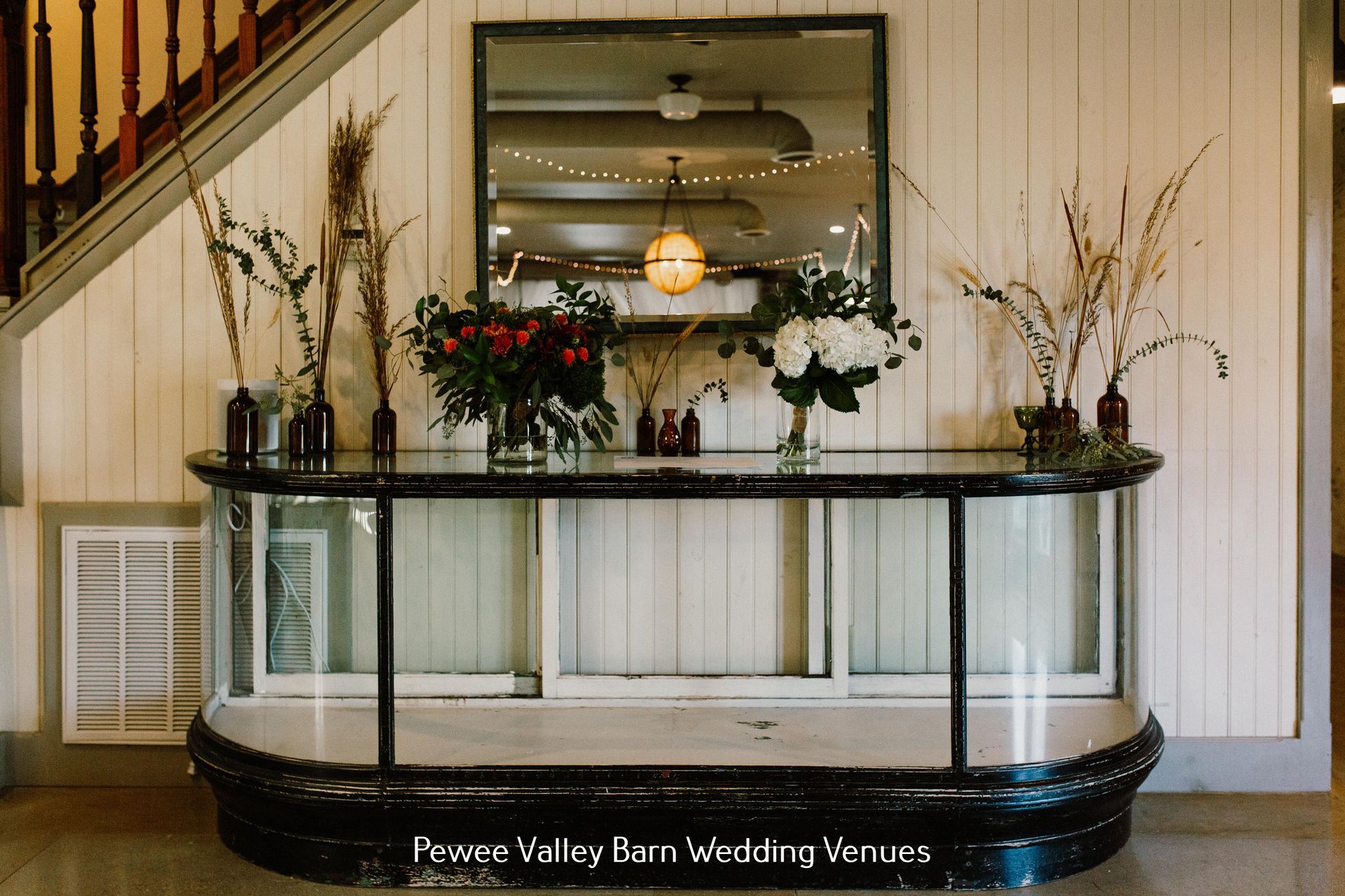 Wedding venue entrance with black glass reception table, flowers, mirror, and white paneled walls