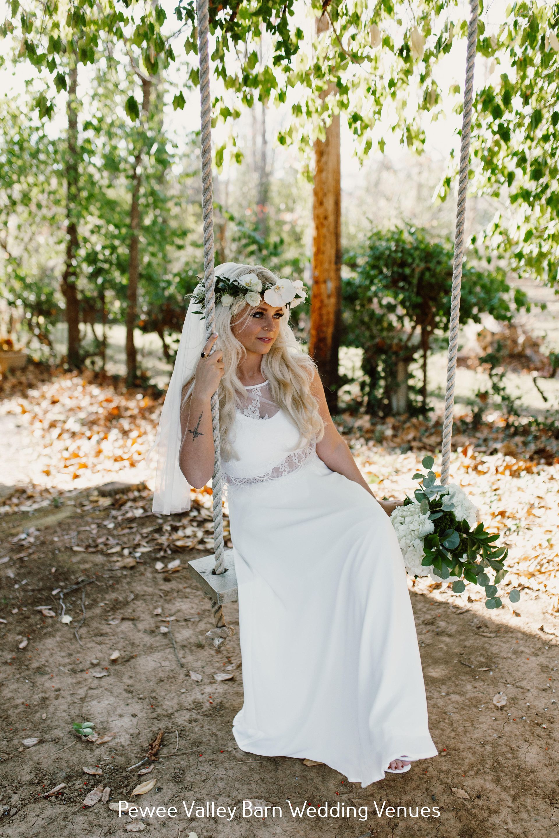 Bride in a white dress and veil seated under a leafy canopy in a sunlit garden