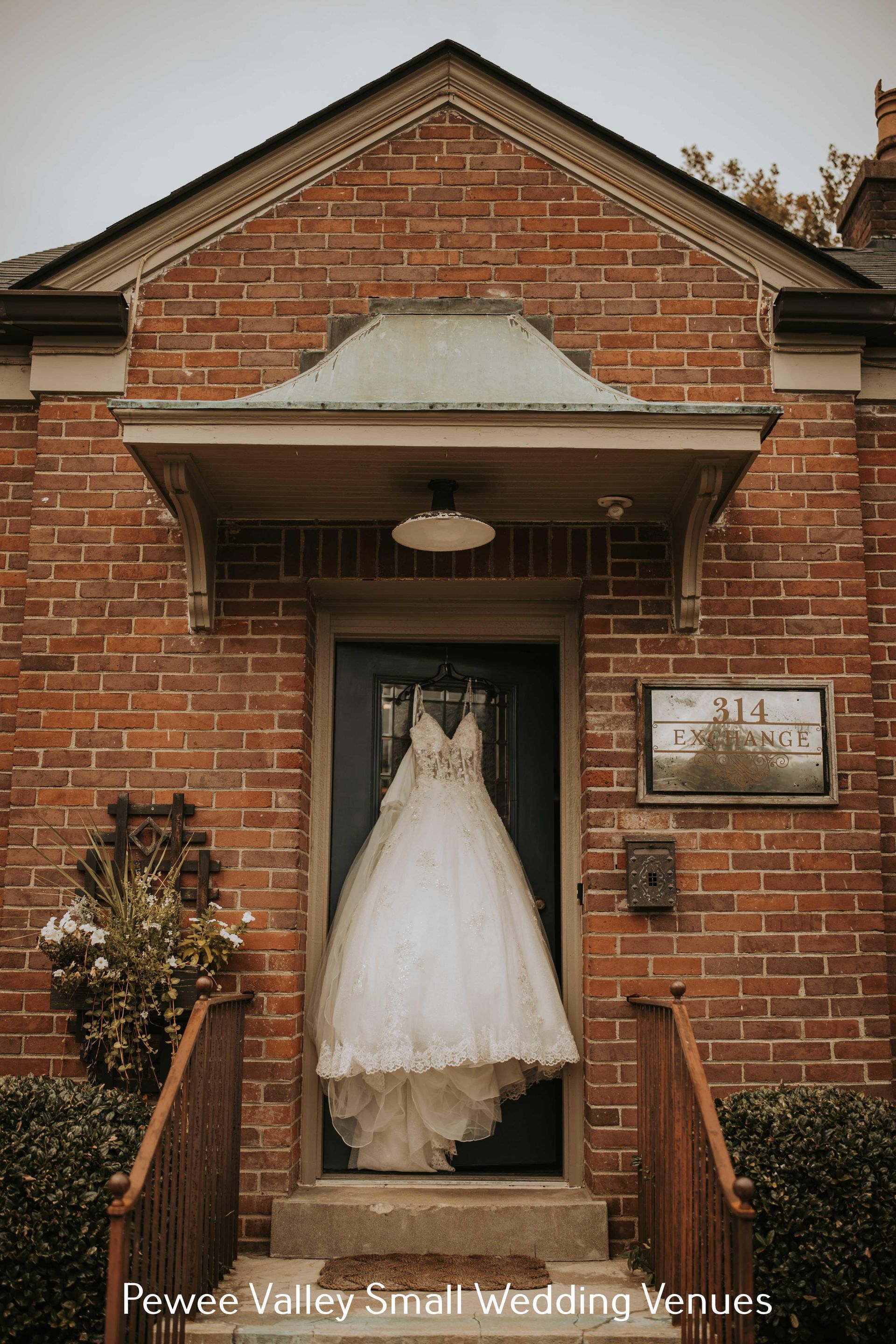 White wedding dress hanging in a brick building doorway with an address plaque nearby