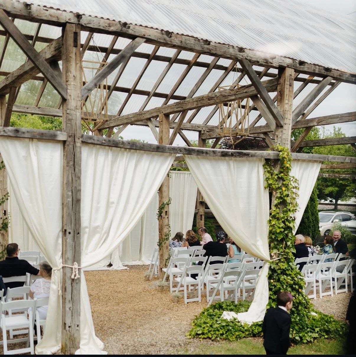 Guests seated under the ivy-draped pavilion as the ring bearer walks the aisle