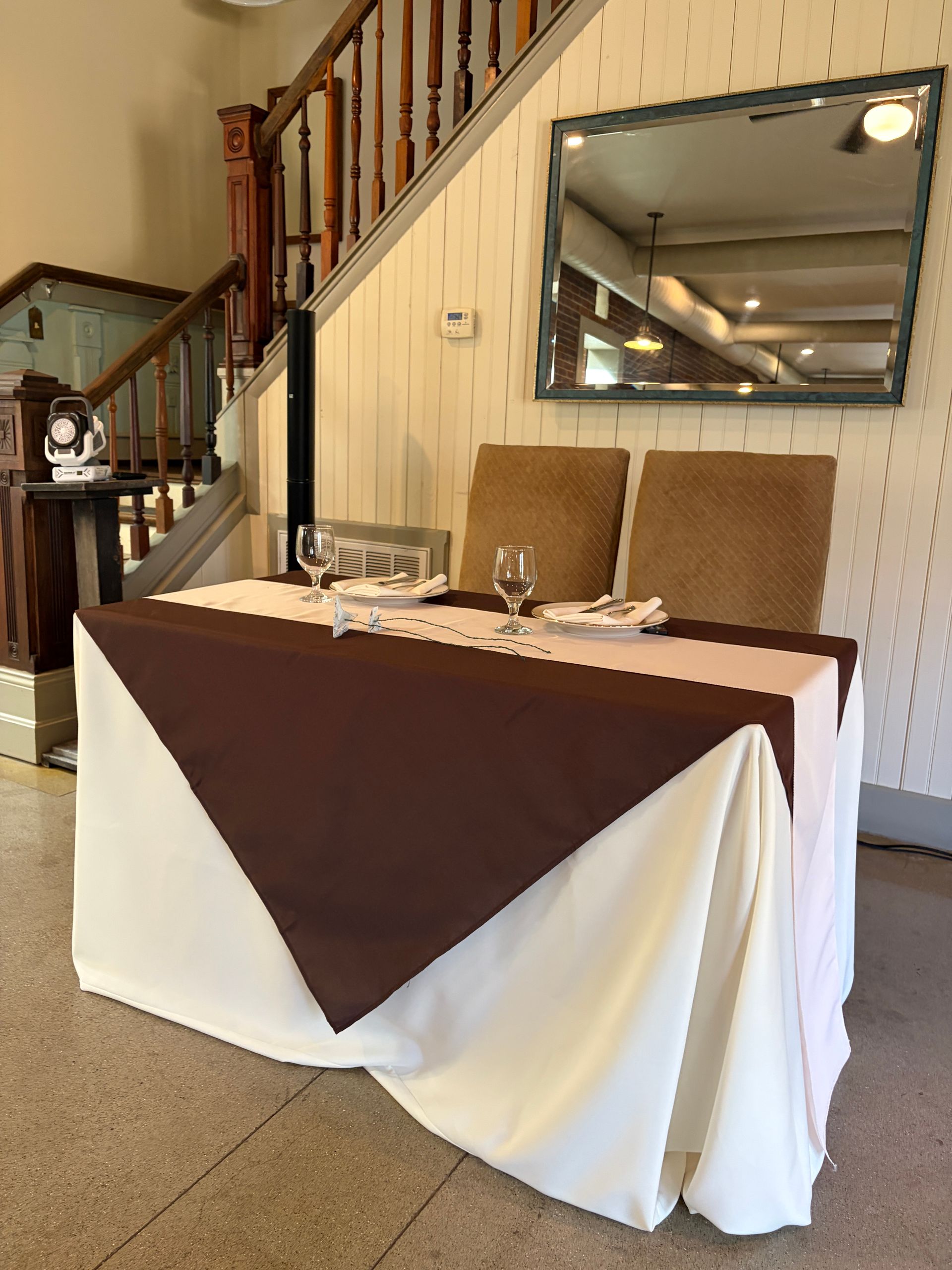 Sweetheart table set with brown and white linen and a mirrored top, no one seated