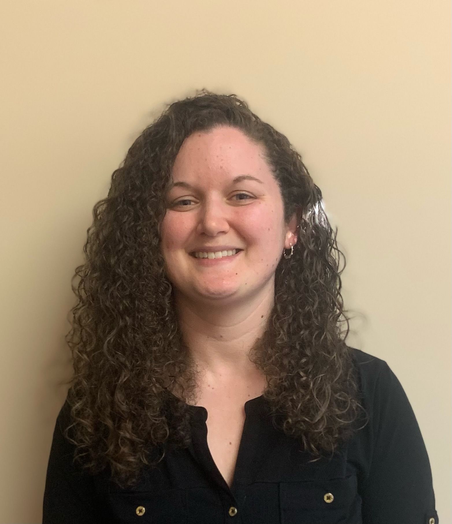 A woman with curly hair is smiling and wearing a black shirt.