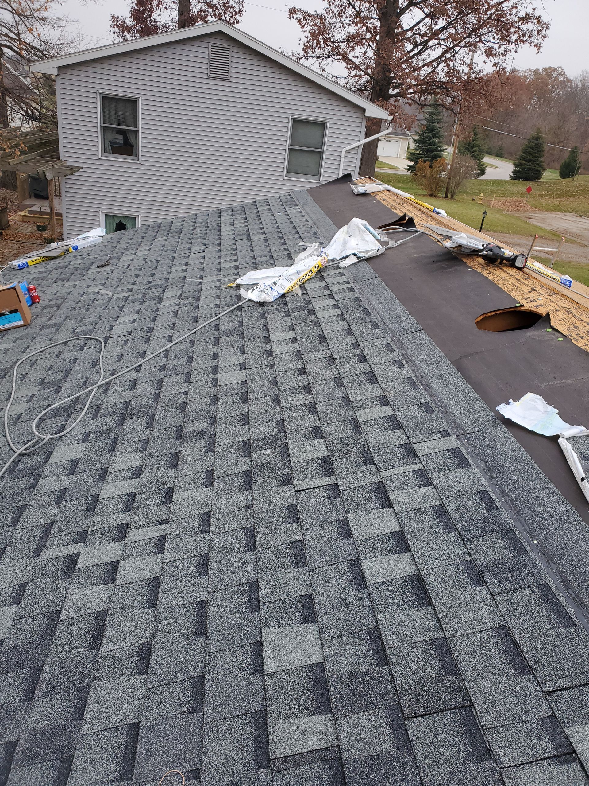 Roof with gray shingles partially installed on a house, underlayment exposed on one section.