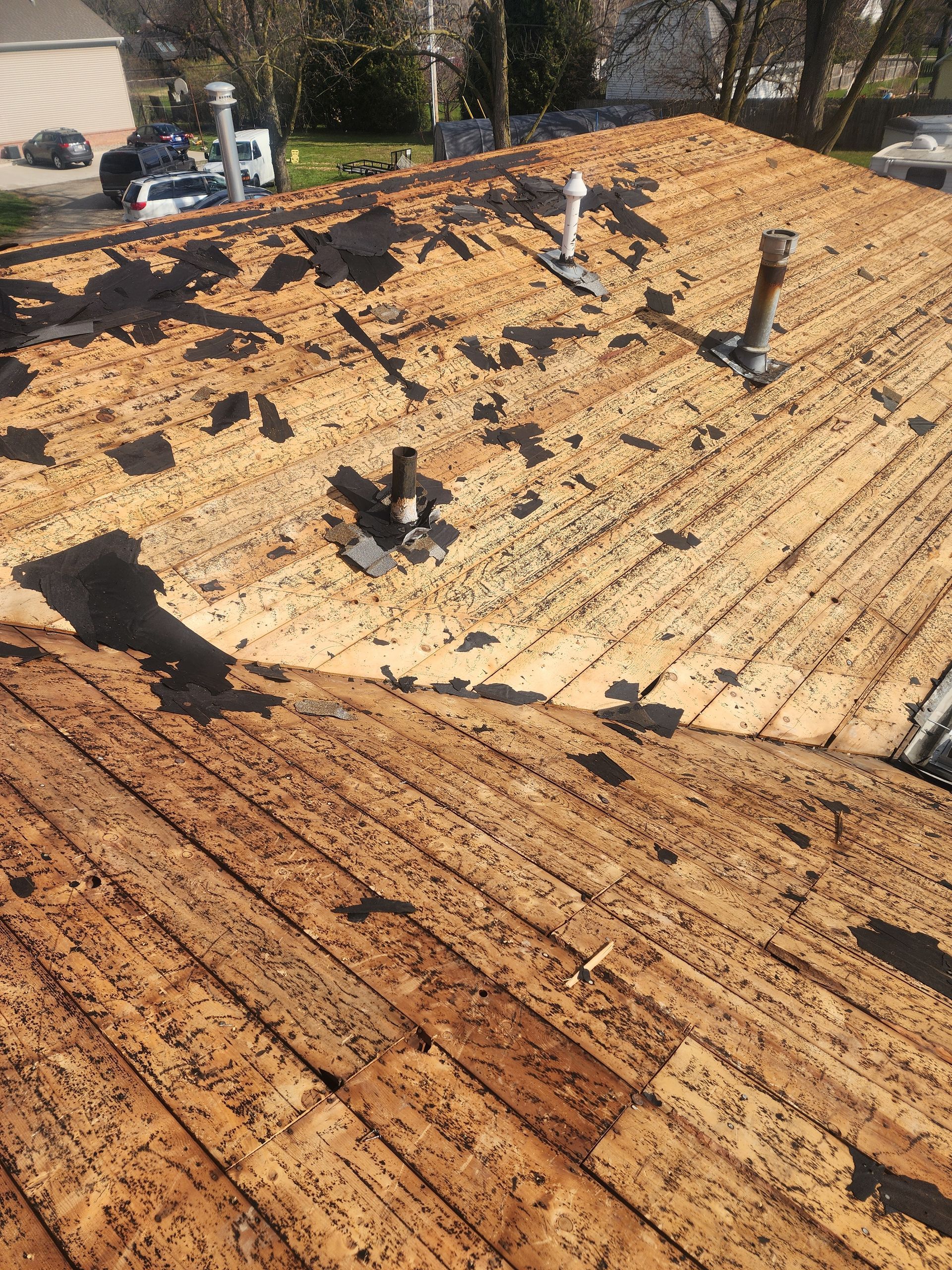Roof with missing shingles, exposing wooden underlayment; sunny outdoor setting.