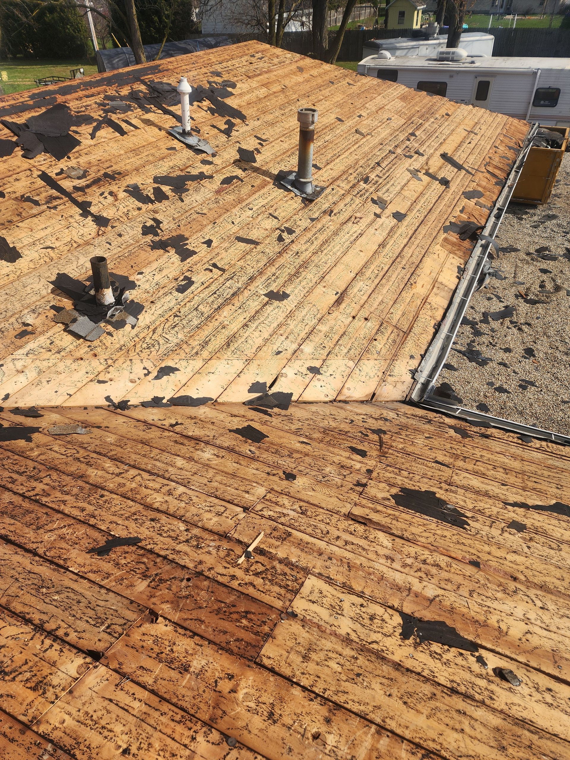 Partially stripped rooftop, revealing wooden sheathing; daylight.