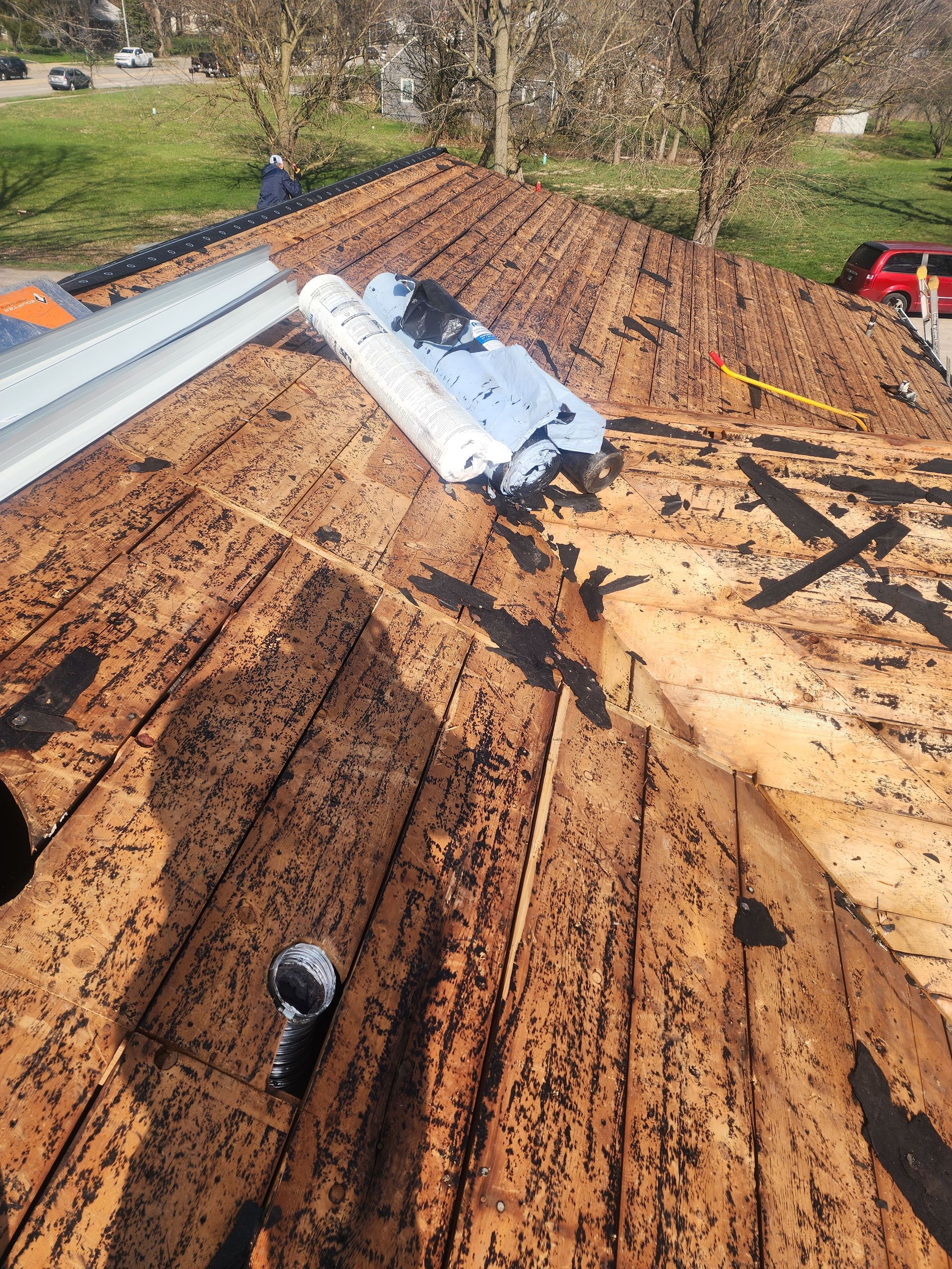 Roof with removed shingles, showing exposed wood, tools, and rolled roofing materials.