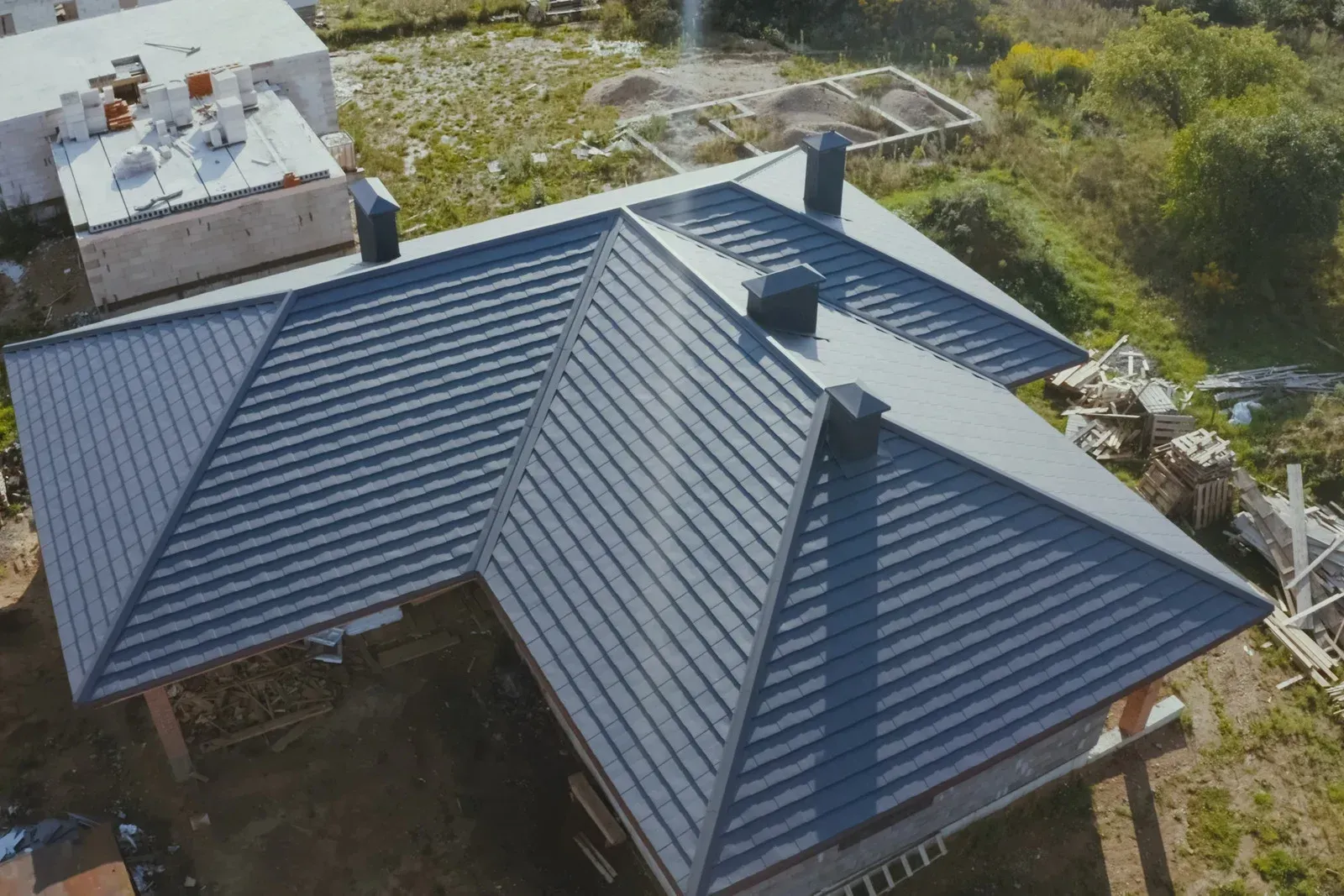 Overhead view of a house with a dark gray metal roof and three black chimneys, set in a grassy area.