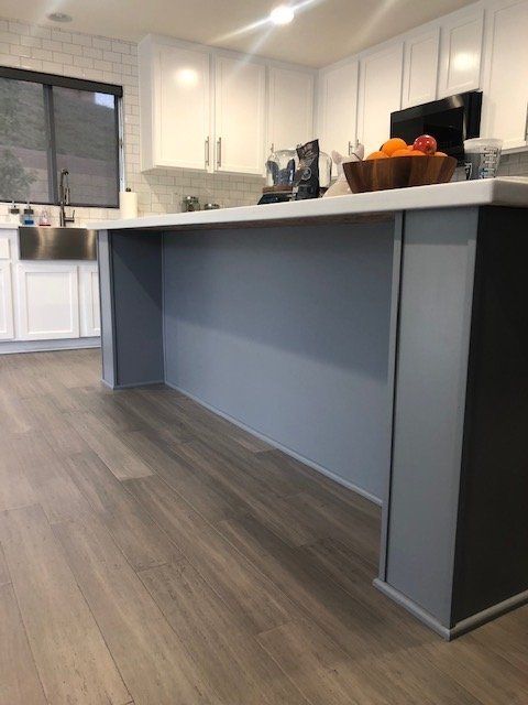 A kitchen island with a smooth, gray base and white countertop, set against a background of white cabinets and wood floors.