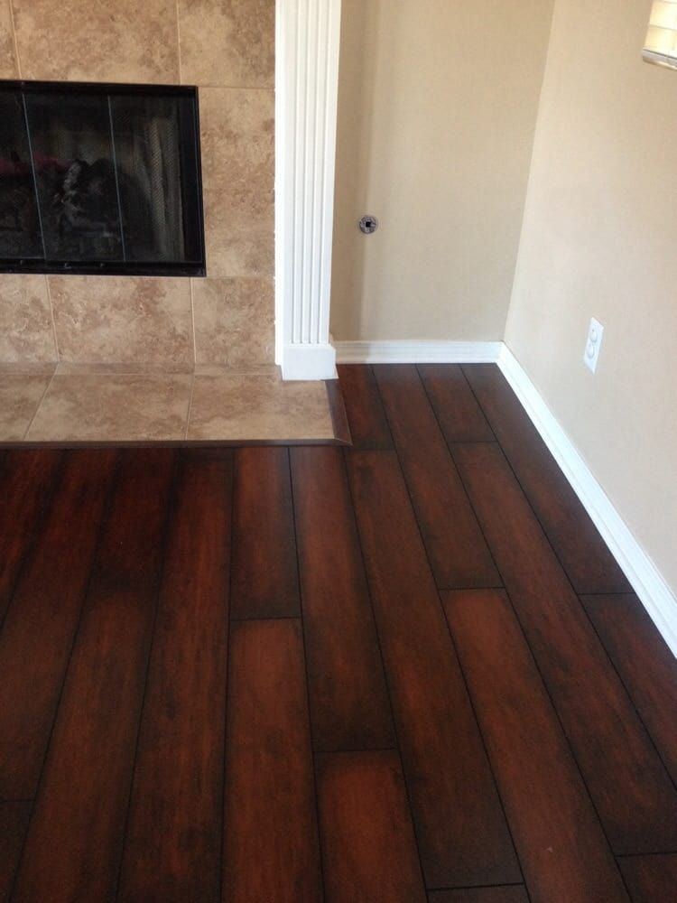 A fireplace with tan tiles next to dark wood-look laminate flooring and white baseboards in a room with beige walls.