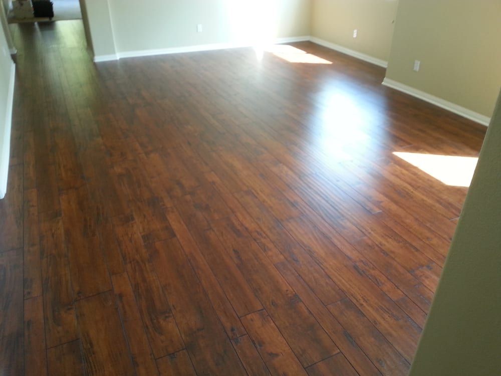 A bright, empty room featuring rich brown wood-look laminate flooring and beige walls with white trim.
