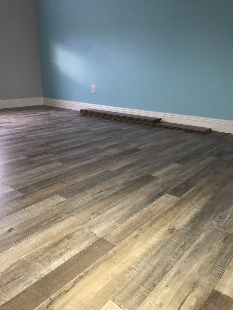 Gray and brown wood-look flooring installed in a room with light blue walls and white baseboards.