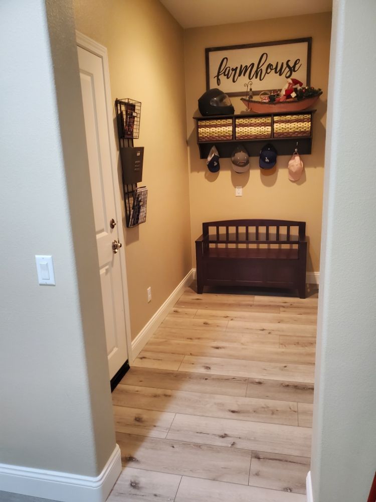 An entryway with light wood flooring, a wooden bench, a wall-mounted coat rack with hats, and a 