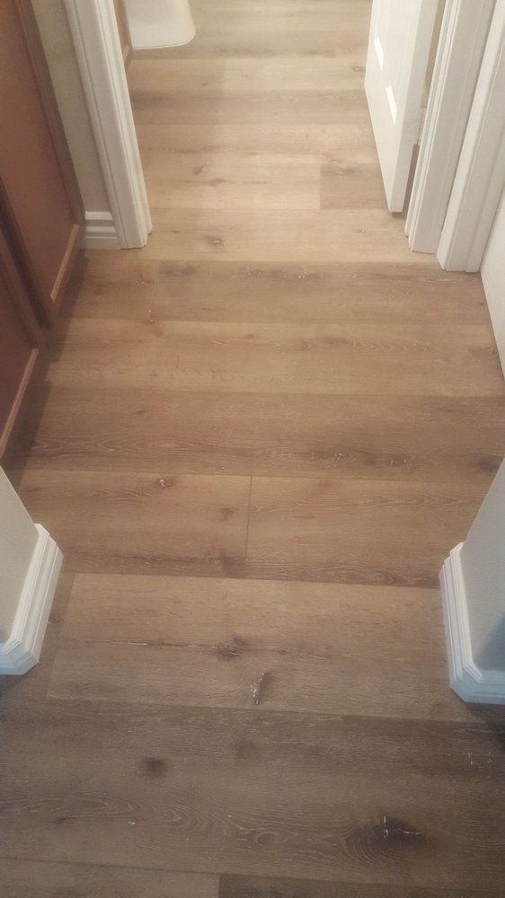 A hallway with light oak-toned wood flooring, leading into a doorway with white trim and baseboards.