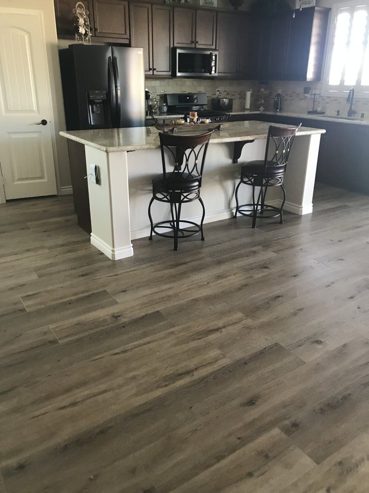 A kitchen with wood-look flooring, a white island with two dark metal bar stools, and dark cabinets.