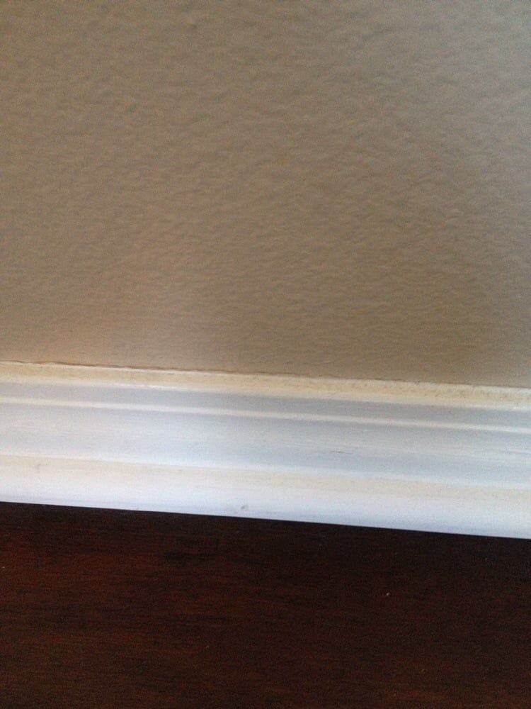 Close-up of white baseboard molding installed against a textured, light beige wall and dark hardwood floor.