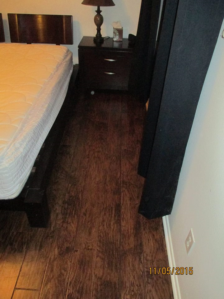 A bedroom corner featuring a dark wood bed frame, a matching nightstand with a lamp, and dark curtains against white walls.