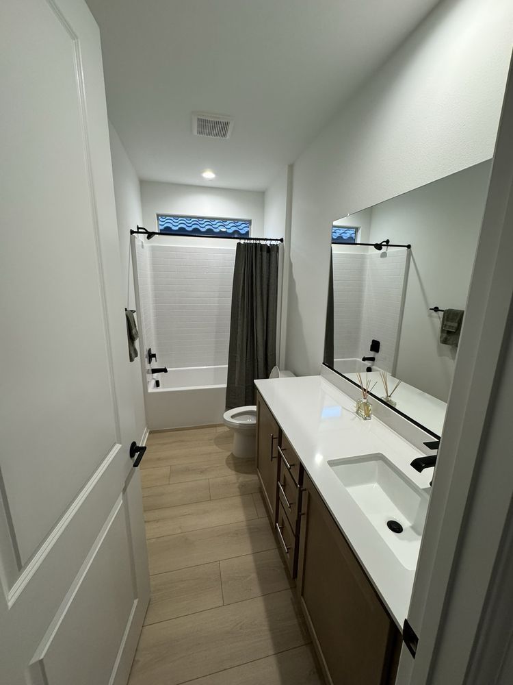A modern bathroom featuring a wood vanity with a white countertop, large mirror, and a walk-in shower with a gray curtain.