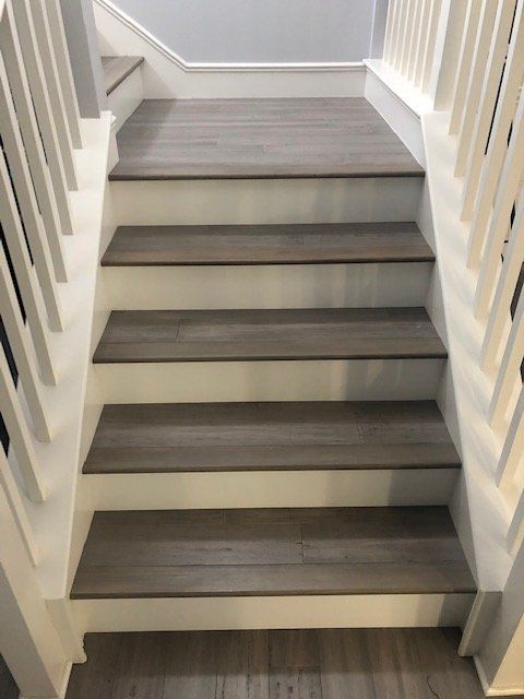 Staircase with grey wood-look treads and white risers, framed by white railings on both sides.